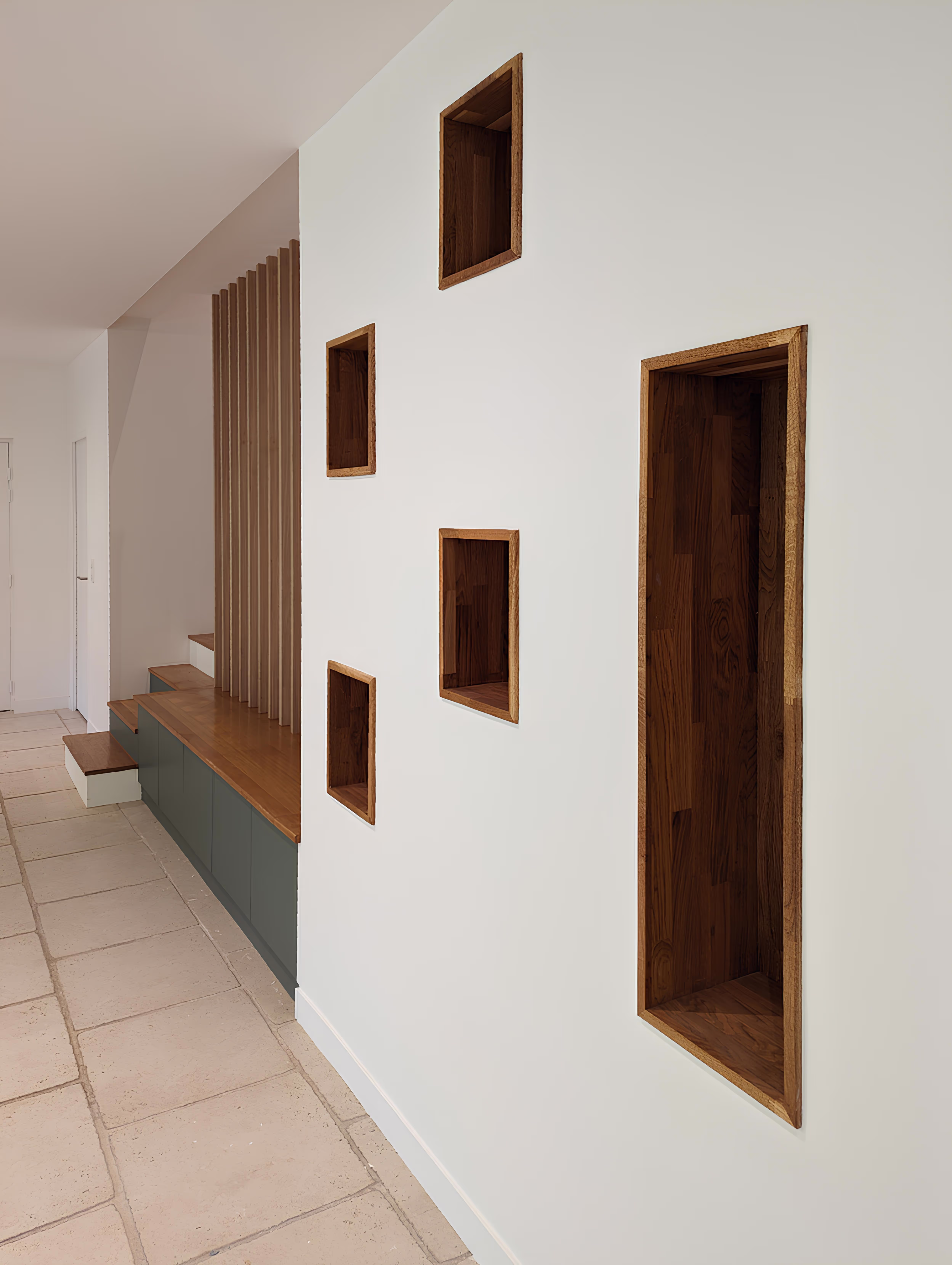 Photographie détaillant les niches décoratives en bois intégrées dans un mur blanc, à proximité de l’escalier, projet Longère de la Messe par SINA Architecture.