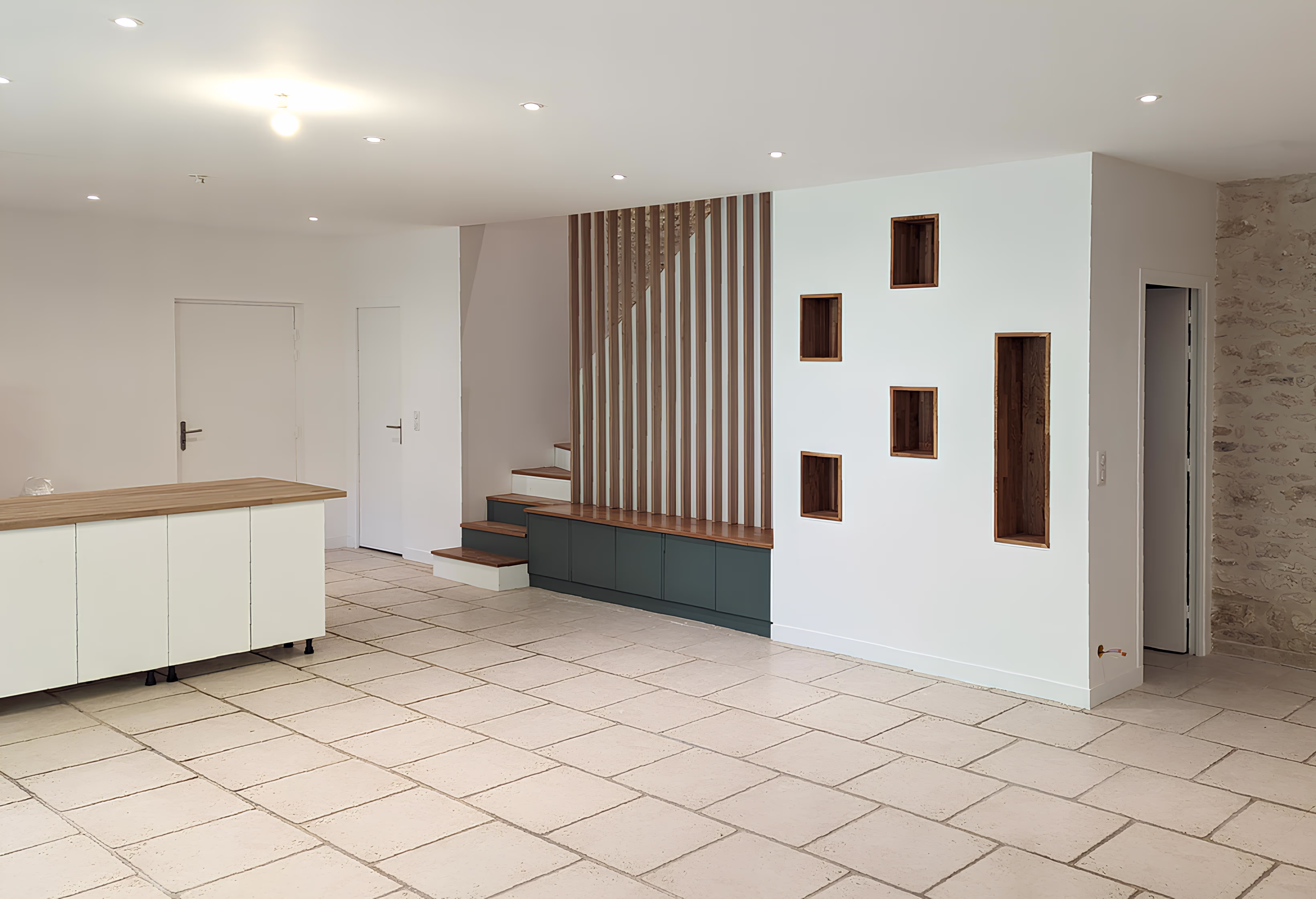 Photographie d’ensemble du salon-salle à manger avec vue sur l’escalier et le mur décoratif à niches bois, projet Longère de la Messe par SINA Architecture.