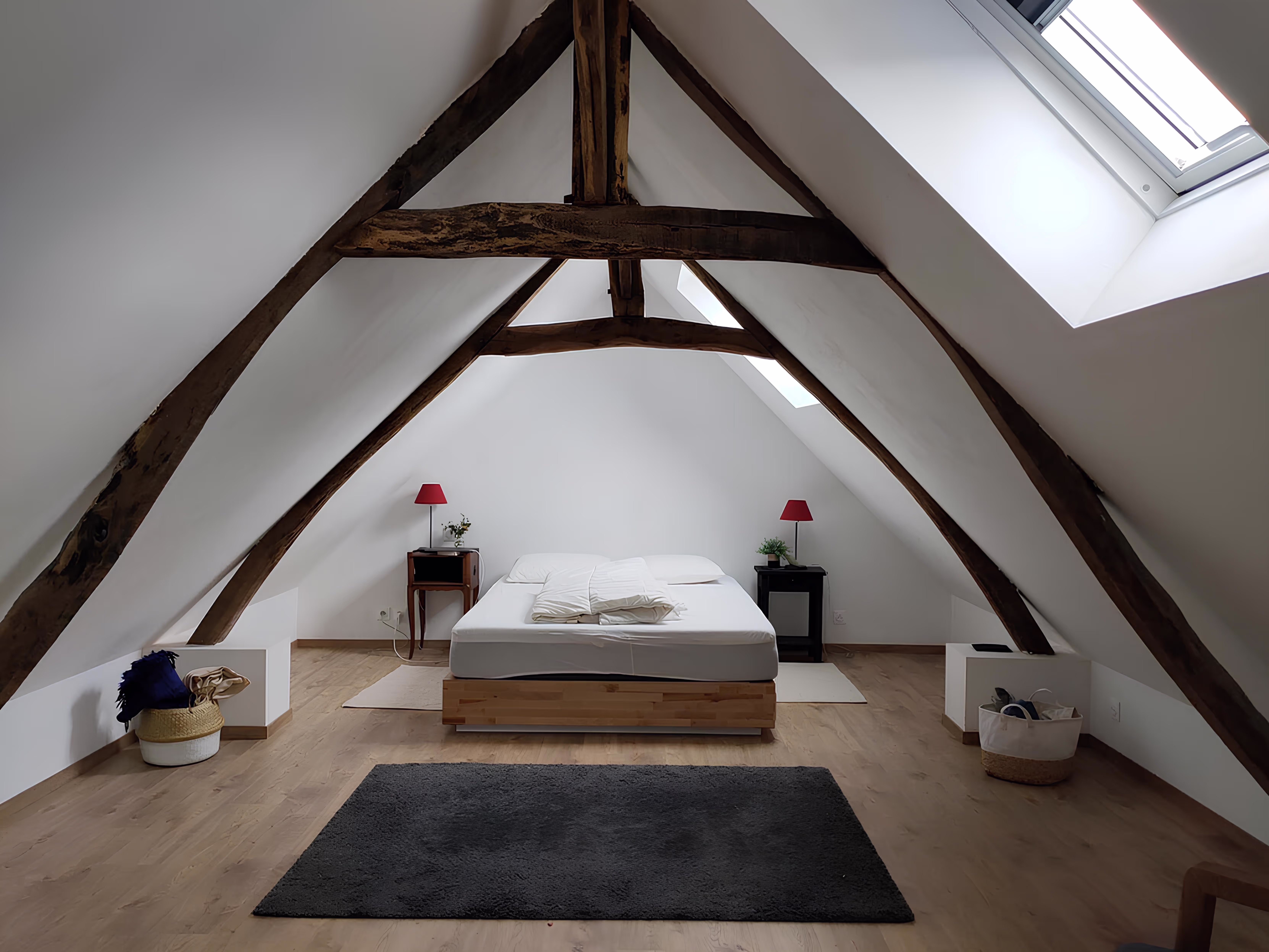Suite parentale mansardée avec dénivelé intérieur et poutres en bois authentiques, rénovation intérieure par SINA Architecture pour la longère Larronville.