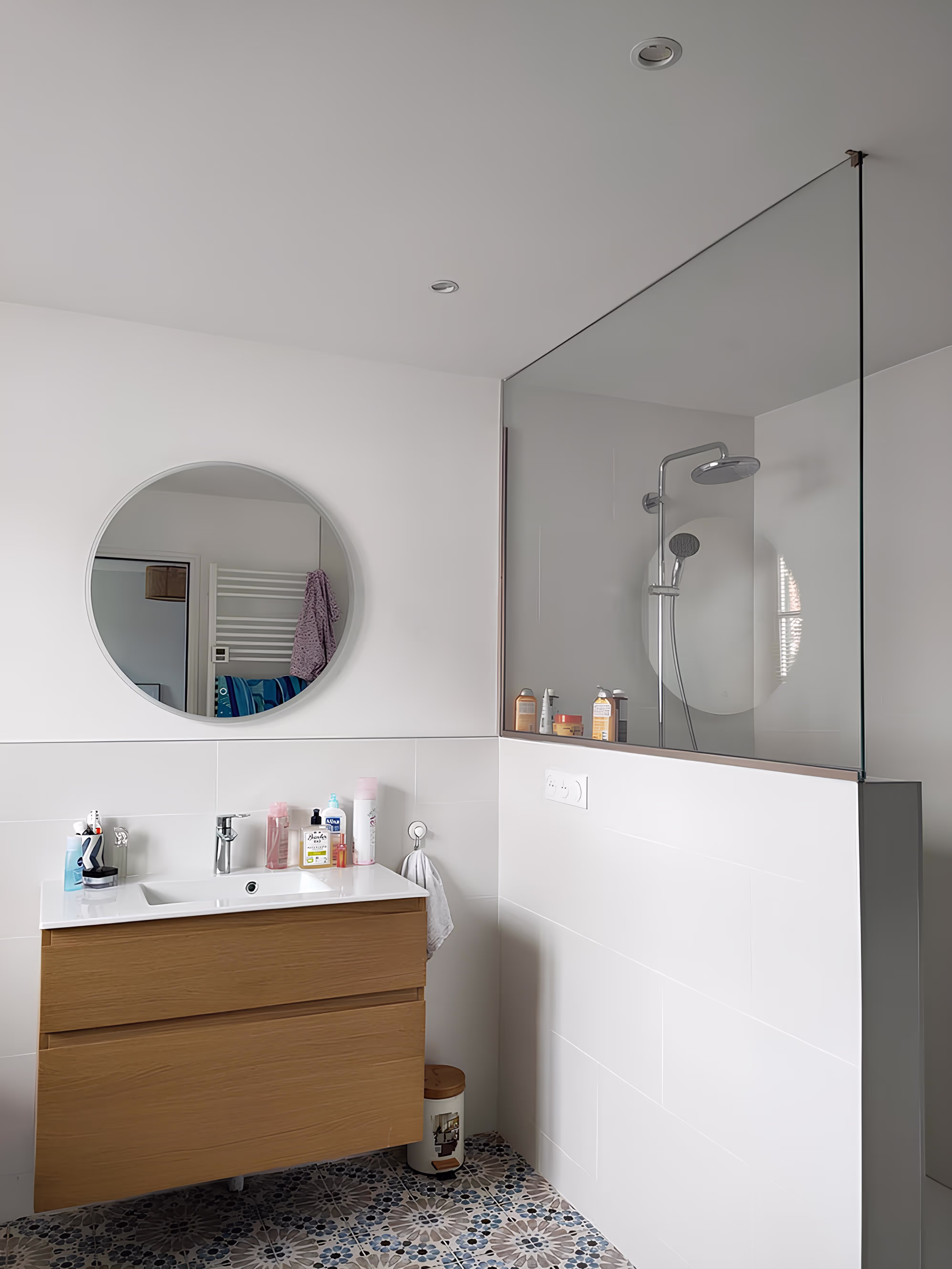 Salle de bain rénovée par SINA Architecture dans la Longère Larronville avec douche à l’italienne, cloison vitrée et miroir rond contemporain.